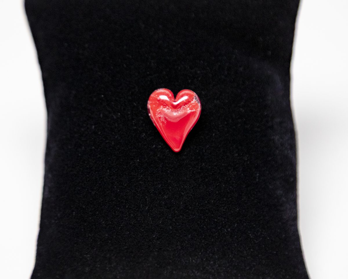 A red glass heart pin on a black velvet pillow