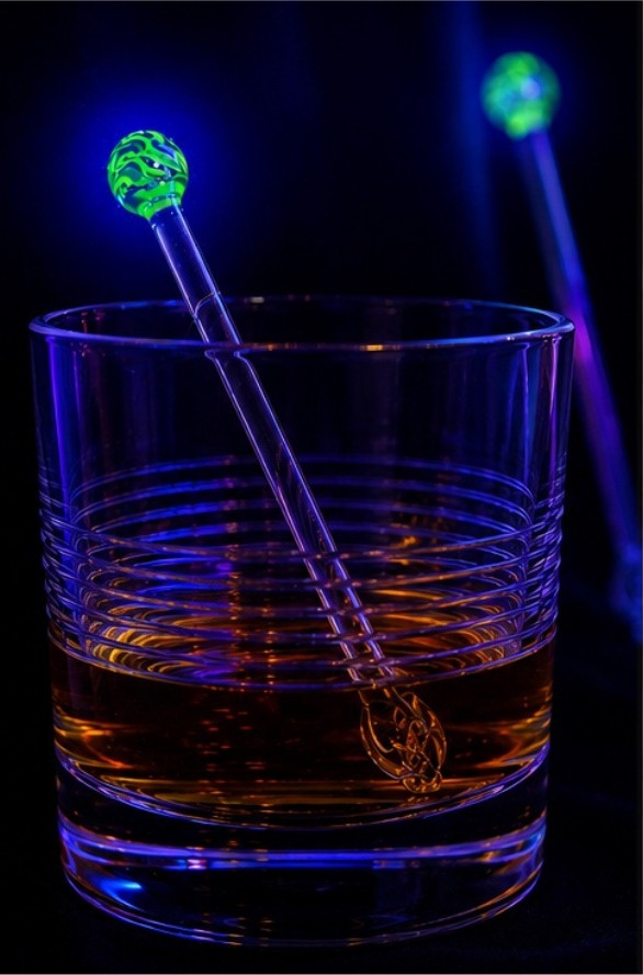 The same glass swizzle stick glowing green and blue under a UV light