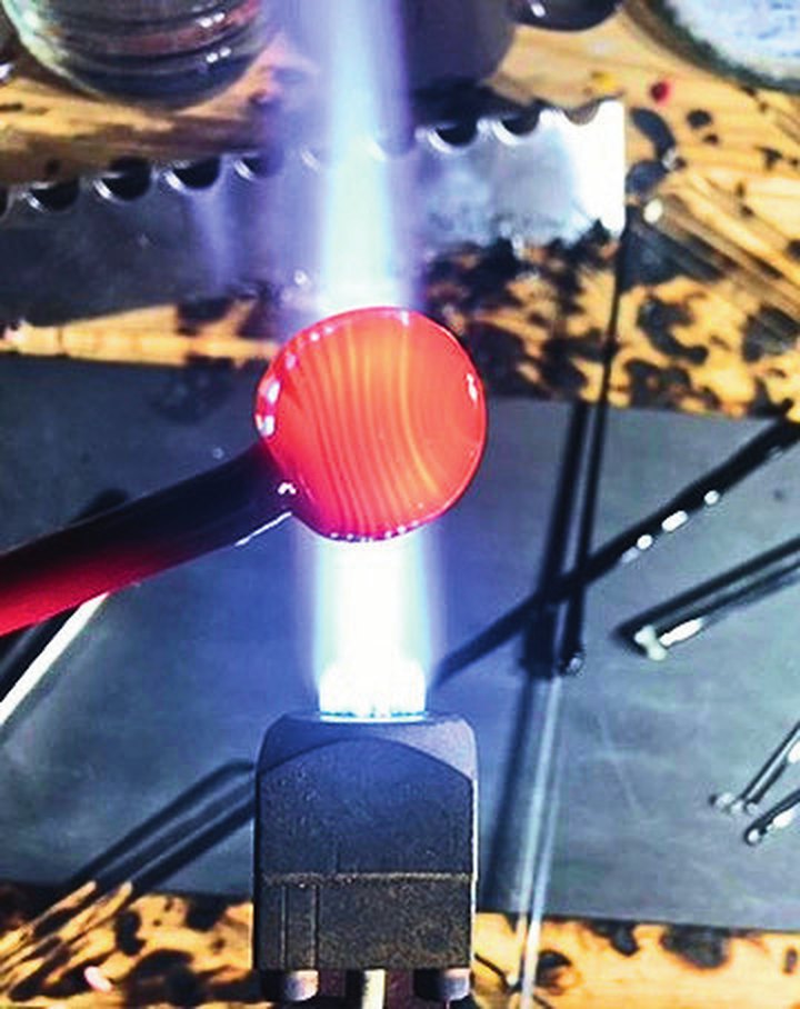A glowing round gather of red glass on the end of the rod