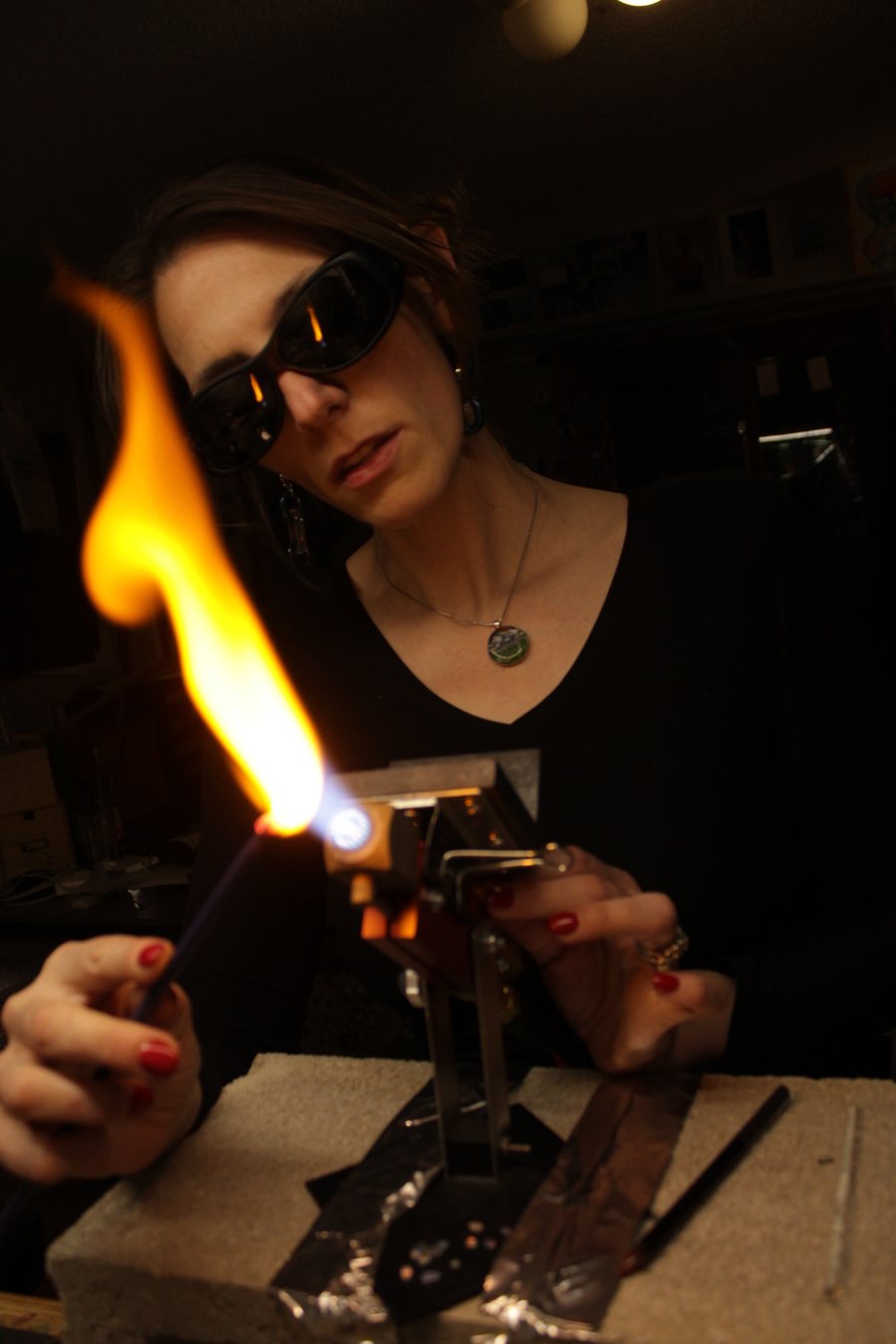Linda Harman at her torch in the studio, a tall flame in front of her